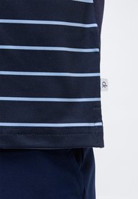 Ύφασμα σκούρου μπλε χρώματος με ανοιχτό μπλε οριζόντιες ρίγες, δείχνοντας ραμμένη τσάκιση και μια μικρή λευκή ετικέτα με τη μάρκα "ck" στο πλάι.