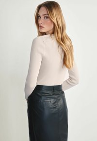 Prążkowana, jasnobeżowa bluzka z długim rękawem o dopasowanej sylwetce; zestawiona z ciemną skórzaną spódnicą o kroju ołówkowym z tylnymi kieszeniami i gładką fakturą.