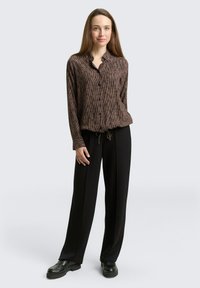 Braun gestreiftes Hemd mit Knopfverschluss, lockerer Passform und Kordelzug am Saum, kombiniert mit weiten schwarzen Hosen und klobigen schwarzen Schuhen.