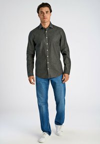 Mörkgrå skjorta med knappar och en bomullstextur, kombinerad med blå jeans och vita sneakers. Har en krage och kontrasterande knappar.