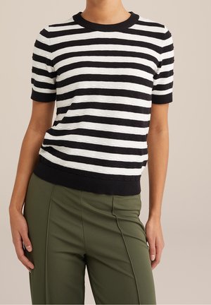 Sort og hvid stribet striktop med korte ærmer, ribbet rund halsudskæring og tekstureret stof, kombineret med grønne skræddersyede bukser.