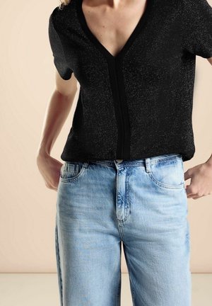 Czarny top z krótkim rękawem, dekoltem w serek i teksturowanym wykończeniem, zestawiony z jasnoniebieskimi jeansami o klasycznym, pięciokieszeniowym kroju.