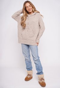 Beżowa oversize'owa bluza z kapturem ze sznurkami i kieszenią z przodu, w zestawieniu z jasnoniebieskimi dżinsami i beżowymi kozakami z futrzaną wyściółką.