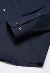 Camicia blu navy con bottone a pressione, caratterizzata da una superficie liscia, maniche lunghe, bottoni argentati e orlo cucito. Il colletto ha bordi arrotondati.