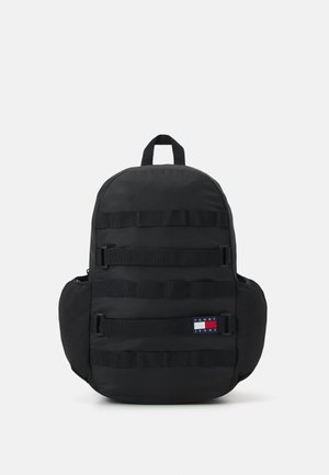 Zaino nero con una texture liscia, dotato di diverse cinghie orizzontali, tasca laterale e un piccolo etichetta di marca in rosso, bianco e blu.