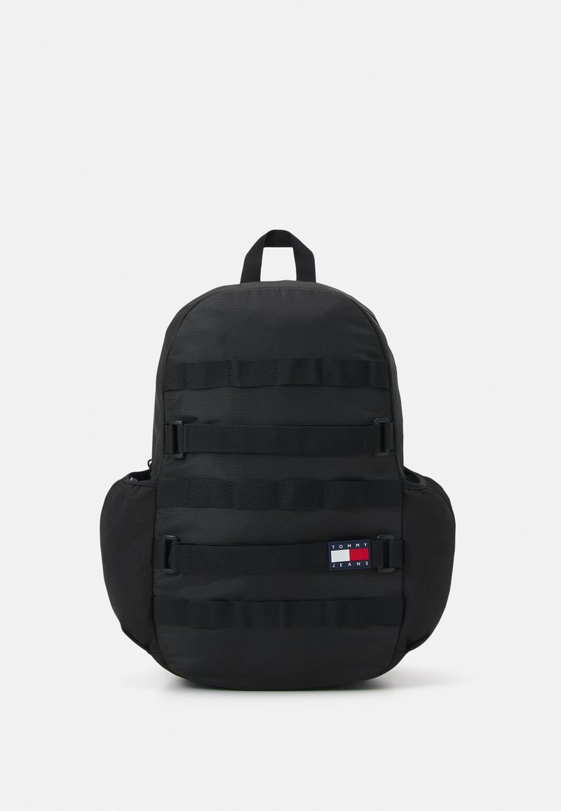 Zaino nero con una texture liscia, dotato di diverse cinghie orizzontali, tasca laterale e un piccolo etichetta di marca in rosso, bianco e blu.