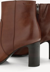 Braune Leder-Stiefeletten mit glatter Oberfläche, ausgestattet mit einem Reißverschluss und einem stabilen schwarzen Blockabsatz. Dezentes geprägtes Branding.