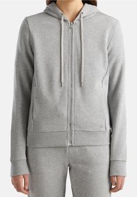 Sudadera gris con cremallera hecha de un tejido suave, con puños y dobladillo acanalados, que presenta una capucha con cordón y dos bolsillos laterales. Diseño sencillo.