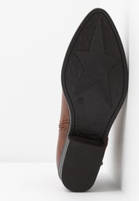 Semelle d'une botte en cuir marron montrant une semelle extérieure en caoutchouc noir avec un grand motif étoile et un talon texturé, taille 37 marquée sur la semelle.