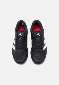 Ζευγάρι μαύρα αθλητικά παπούτσια με λευκές ρίγες, διχτυωτό πάνω μέρος, μαύρα κορδόνια και κόκκινα εσωτερικά πέλματα σε λευκό φόντο.