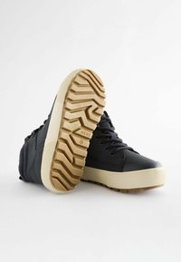 Czarne sportowe buty za kostkę z teksturowanym wierzchem, gumową podeszwą i kontrastującą brązową podeszwą. Posiada okrągłe sznurówki i minimalne logo.