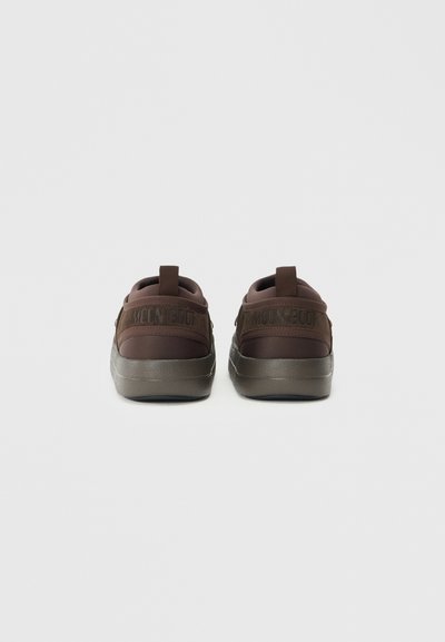 Zapatillas marrones con una parte superior suave y texturizada y una suela oscura en contraste. Presenta una tira de agarre y una marca en relieve en el talón.