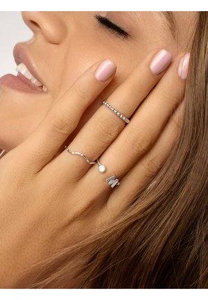 Cuatro anillos de plata en una mano, con un diseño ondulado suave, una banda con cuentas, un acento de puntos y una letra "M" grabada.
