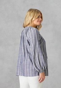Blusa a righe blu e bianche con scollo arricciato, maniche lunghe e vestibilità rilassata. Realizzata in tessuto leggero con una texture liscia.