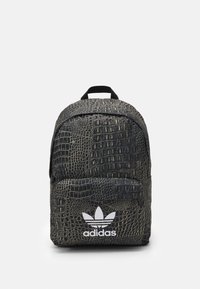 Svart ryggsäck med krokodilsmönster, framficka med dragkedja och vit Adidas-logotyp. Har ett handtag upptill och vadderade axelremmar.