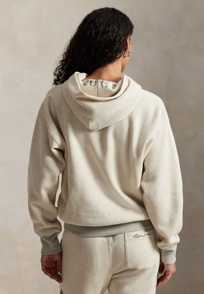 �Μπεζ φούτερ με μαλακή υφή, διαθέτει διπλή κουκούλα και ριγέ μανίκια. Σημαντική λεπτομέρεια λογότυπου στη μέση.