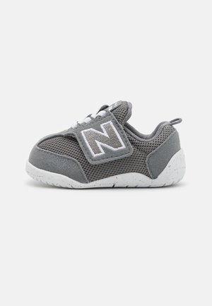 Pequeña zapatilla para niño pequeño en gris y blanco con tejido de malla, tira de velcro con una gran "N" y suela blanca con motas.