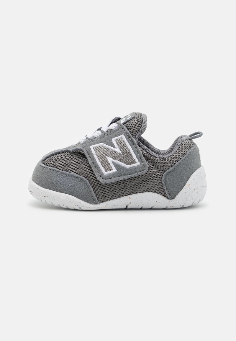 Petite chaussure de sport pour tout-petit en gris et blanc avec tissu en maille, bride à scratch ornée d'un grand "N" et semelle blanche tachetée.