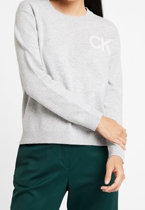 Lichtgrijze gebreide trui met een ronde halslijn, geribde manchetten en zoom. Beschikt over een subtiele "CK" logo op de borst. Gecombineerd met groene broek.