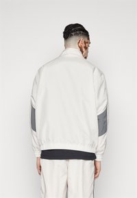 White bomber jacket with gray accents, elastic cuffs and hem, smooth texture, high collar, and a relaxed silhouette. Back view.