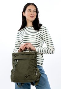 Oliviroheline seljakott tekstureeritud kangaga, ülemise tõmblukuga, kahe küljetaskuga ja esiklapiga, millel on SFY logo.