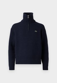 Navyblauwe gebreide trui met een hoge kraag en een halve rits, voorzien van een gestructureerd patroon en een klein Lacoste-logo op de linkerborst.