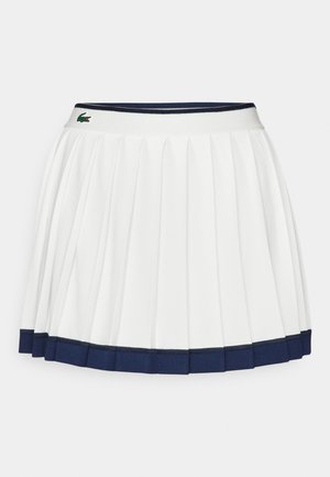 White pleated skirt with a navy blue waistband and hem. Features soft fabric with horizontal stripes on the waistband, designed for comfort.