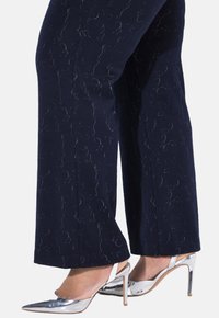Marinblå byxor med ett subtilt dekorativt mönster och en stilren, rak ben-design, i kombination med silverfärgade lackskor med klack.
