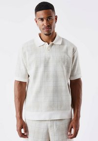 Gestructureerde polo met korte mouwen in lichtbeige met een subtiele ruitpatroon, contrasterende witte kraag en zoom, voorzien van een knoopsluiting.
