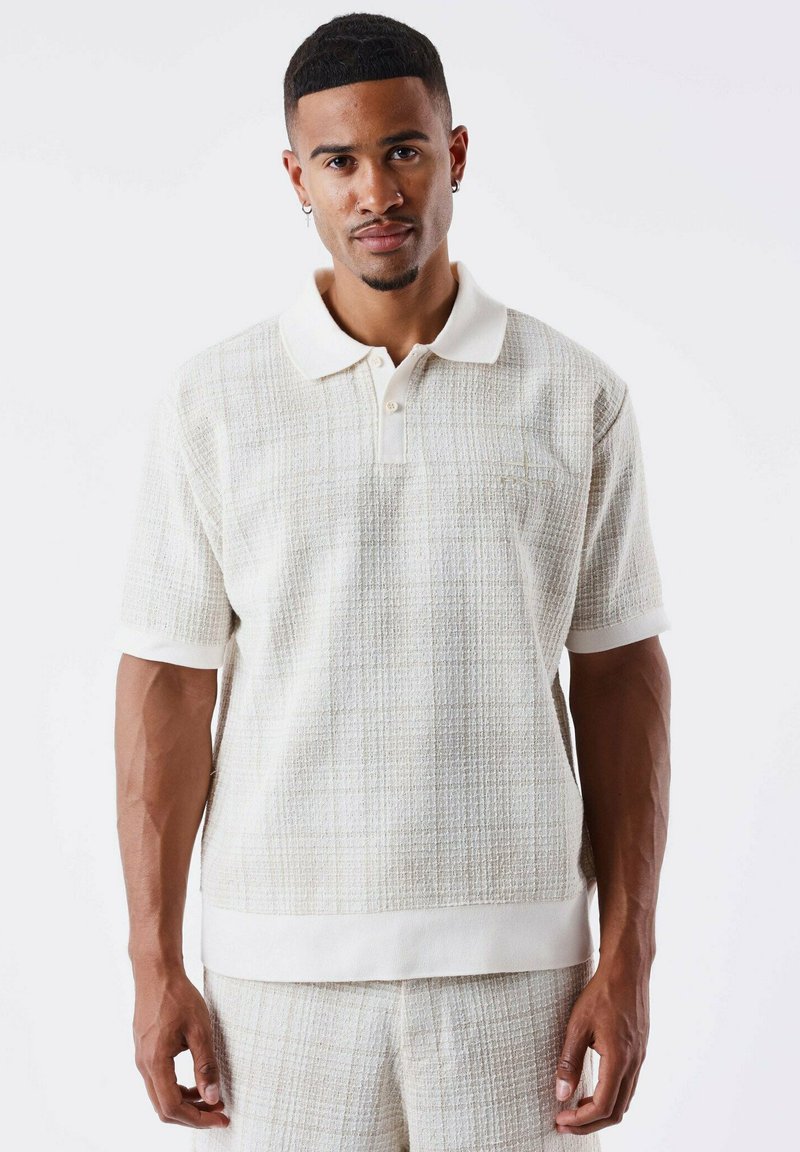 Gestructureerde polo met korte mouwen in lichtbeige met een subtiele ruitpatroon, contrasterende witte kraag en zoom, voorzien van een knoopsluiting.