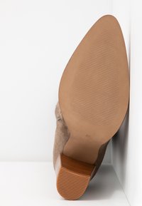 Zapato de tacón alto de ante marrón con punta redondeada, suela texturizada y acento de aspecto madera en el tacón. Talla 37 marcada en la suela.