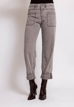 Person wearing gray cropped jeans with cuffed hems and black high-heeled ankle boots against a plain background.