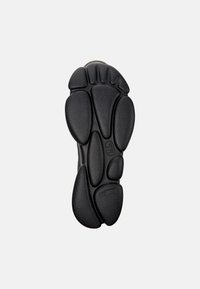 Suela de zapato de goma negra con un diseño orgánico y redondeado, adornada con patrones texturizados y secciones distintas en forma de cápsula para mayor tracción.