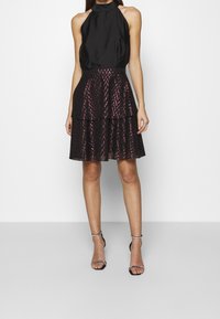 Svart halterneck-klänning med ett lager av kjolar som har ett zigzag-mönster i svart och rosa. Slät tyg med en figurnära midja.