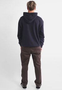 Sweatshirt à capuche bleu marine avec une coupe décontractée, en tissu coton et avec des poignets côtelés, associé à un pantalon marron et des baskets noires.