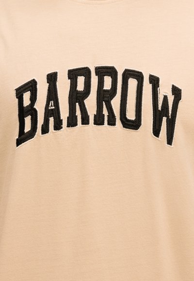 Μαύρο κεντημένο κείμενο "BARROW" με έντονα κεφαλαία γράμματα σε μπεζ υφασμάτινο φόντο.