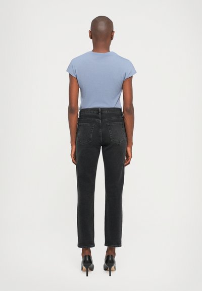 Mørke jeans med rette ben og baklommer, sammen med en tettsittende lyseblå t-skjorte. Svarte heler fullfører antrekket.