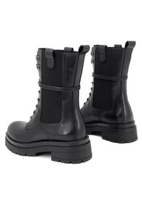 Stivali da combattimento in pelle nera con pannelli elasticizzati laterali, chiusura con lacci, suole robuste e dettagli hardware metallici sottili. Texture liscia.