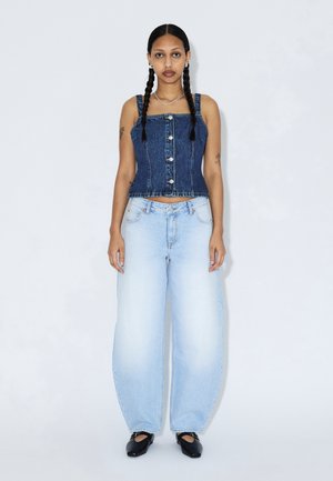 Denim cropped top met een vierkante halslijn en knopen aan de voorkant, gecombineerd met lichtblauwe wijde jeans. Model draagt zwarte platte schoenen. Effen achtergrond.