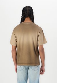 Brun gradient t-shirt med korte ærmer og afslappet pasform. Glat tekstur, rund halsudskæring og minimal design på ryggen.