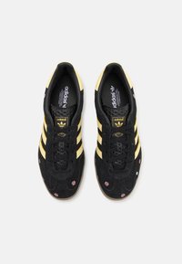 Svarta mockaskor med gula ränder och blommönster, med en texturerad snörning framtill och en gummisul.