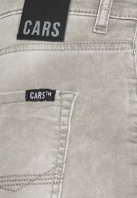 Ljust grå denimjeans med detaljer på bakfickan och två svarta tygetiketter med texten "CARS" som är sydda på fickan och midjan.