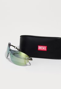 Lunettes de soleil teintées de vert avec un design épuré, des accents en métal et un étui en cuir noir arborant un logo rouge "DIESEL".