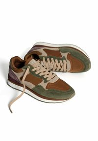 Une paire de baskets en daim marron, beige et vert avec des lacets en tan, des semelles intermédiaires blanches et des semelles extérieures en caoutchouc gris sur un fond blanc.