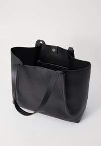 Sac fourre-tout en cuir noir avec une finition texturée, ouvert en haut, anses longues et poche intérieure zippée pour un rangement sécurisé.