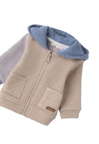 Sudadera con cremallera color beige, capucha azul y mangas grises. Hecha de suave algodón, cuenta con bolsillos frontales y una etiqueta de logo de cuero.