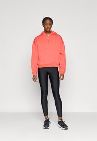 Κοραλλί φούτερ με φερμουάρ και τσέπη καγκουρό, σε συνδυασμό με μαύρο κολάν και μαύρα αθλητικά παπούτσια. Ελαφρύ ύφασμα με άνετη γραμμή.