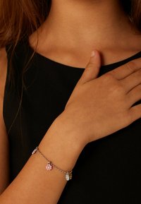 Zilveren kettingarmband met kleine bloemenbedels in roze, paars en blauw, gedragen om een pols tegen een zwarte achtergrond.