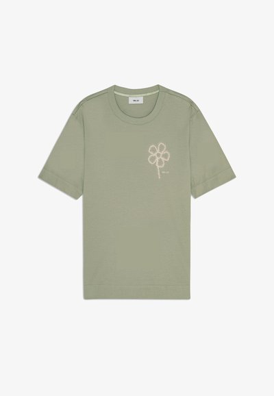 Oliivinvihreä t-paita pehmeää puuvillaa, jossa on vaaleaa kukkataidetta vasemmassa rinnassa. Pyöreä kaula-aukko ja lyhyet hihat.