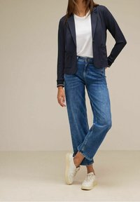 Námořnický blejzr s kapsami, bílý tričko a volné modré džíny. Bílé tenisky s polstrovanou podrážkou. Texturovaný, ležérní design.